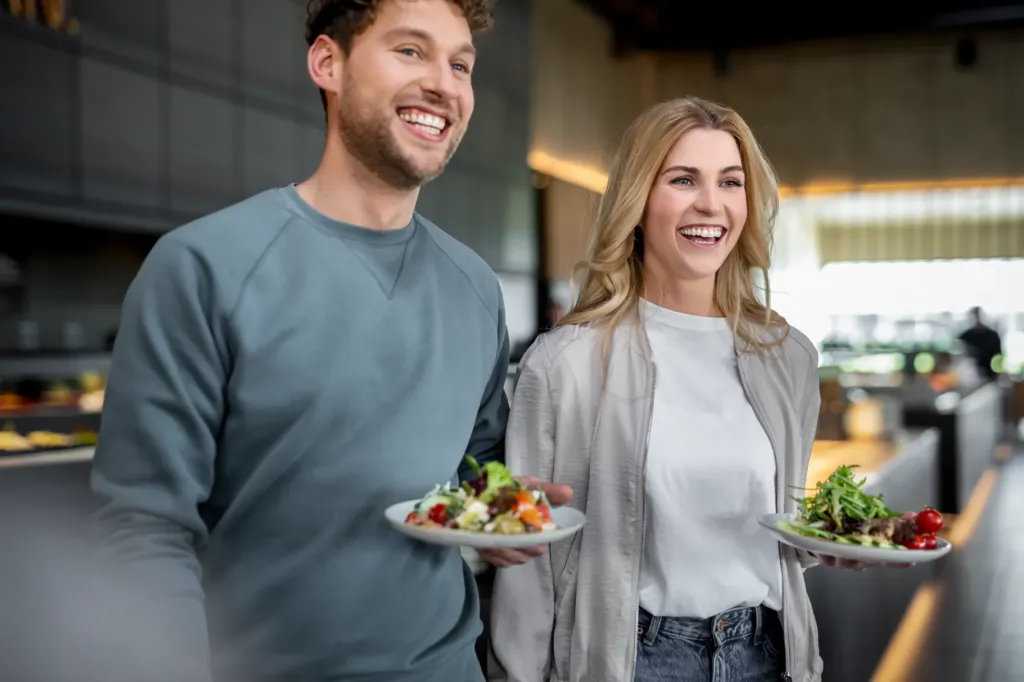 Ein Mann und eine Frau mit gefüllten Tellern vor umfangreichem Erlebnis Buffet