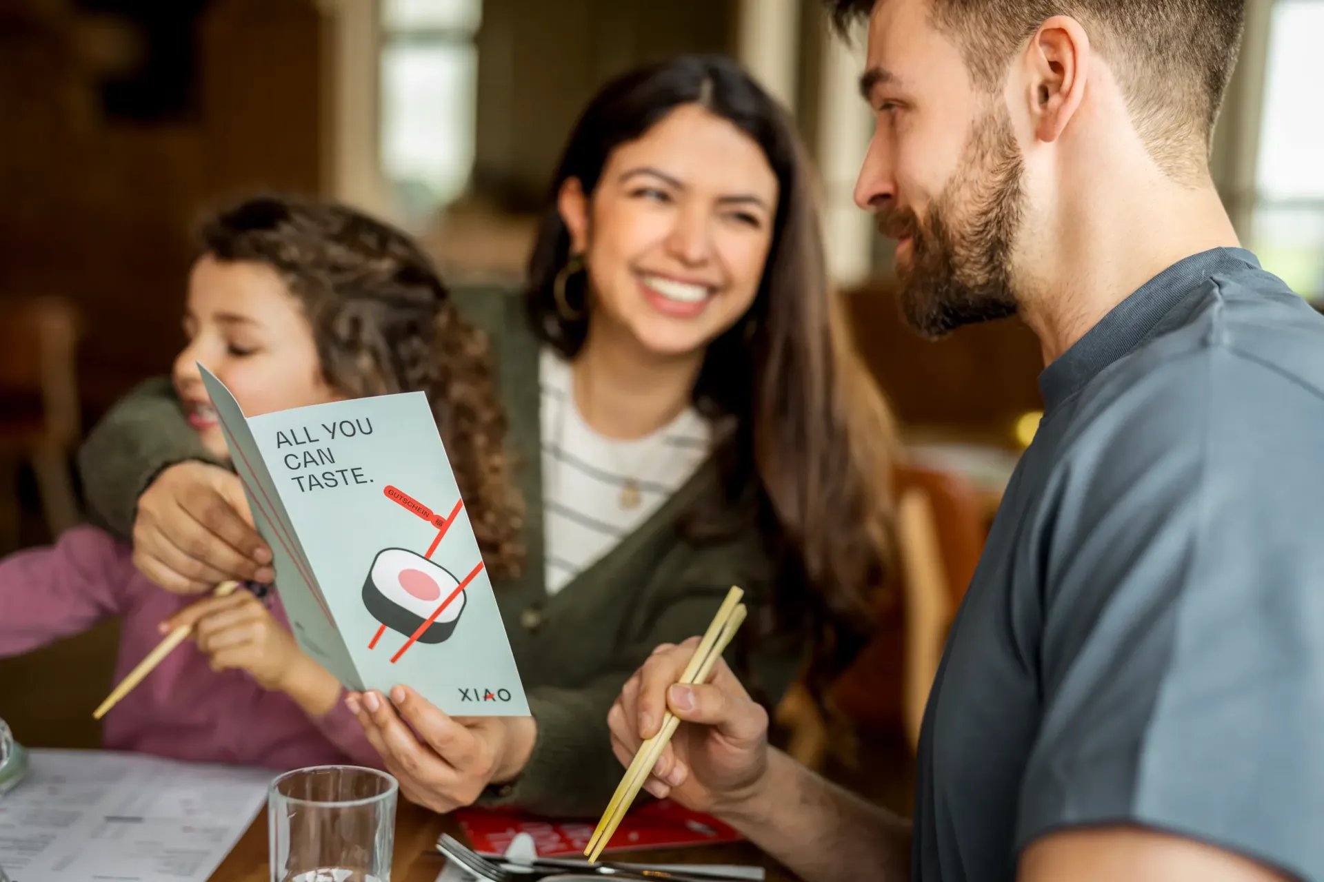 Eine Familie mit Kind liest die stylish designte Speisekarte mit Sushi Grafik und All-you-can-taste Aufdruck