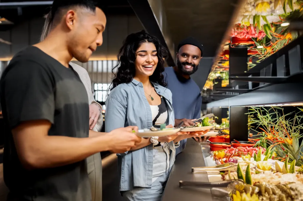 Drei Freunde stellen sich am All-you-can-eat Asia Buffet Teller mit Meeresfrüchten, frischem Fisch, Fleisch und Gemüse zum Grillen zusammen