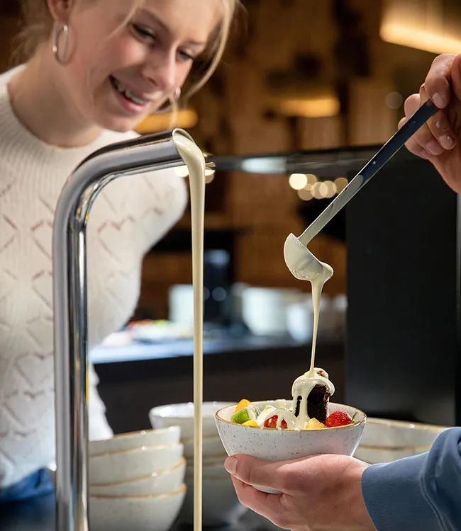 Weiße Schokolade fließt über eine Dessertschale mit Brownie und frischen Früchten