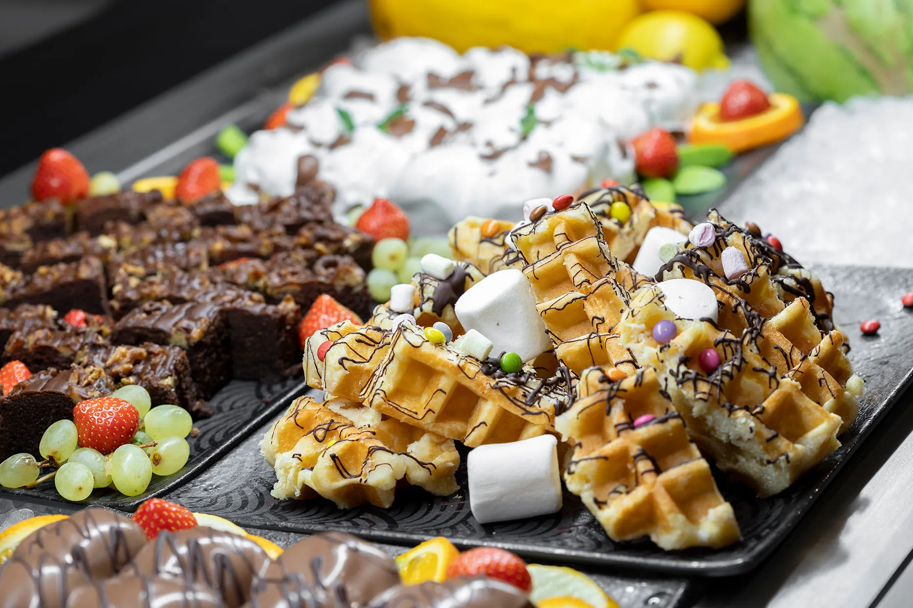 Waffeln mit Schokolade und Marshmallows, Brownies, Erdbeeren und Trauben am Dessertbuffet