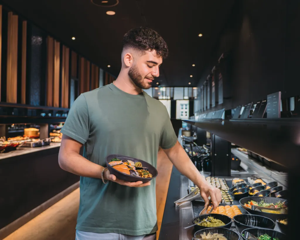 Gast füllt am Buffet eine Take-away-Schale mit warmen Gerichten