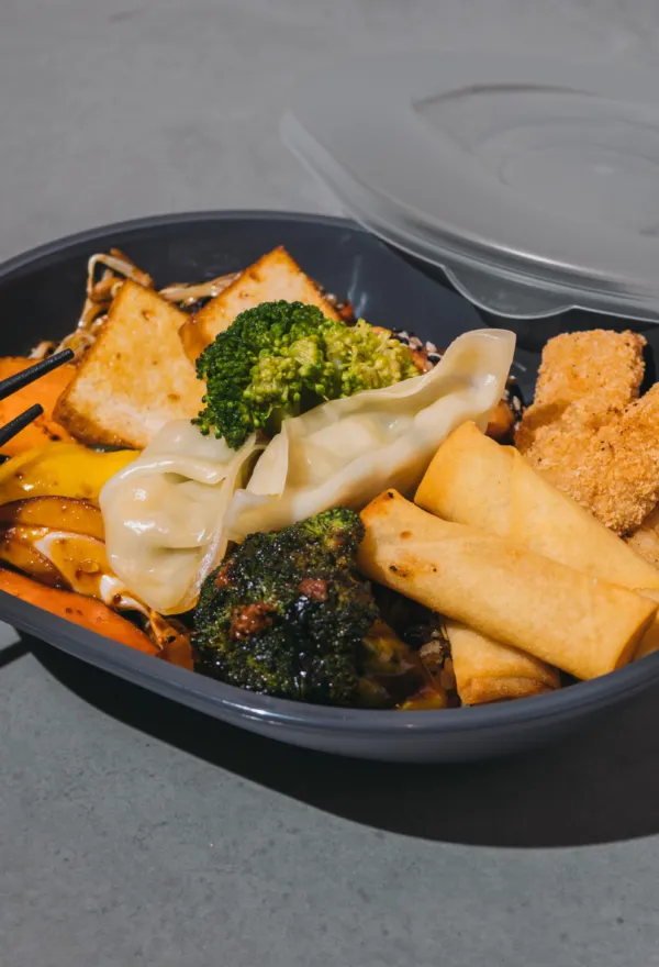 Take-away-Schale mit Frühlingsrollen, Teigtaschen, Brokkoli und Gebackenem