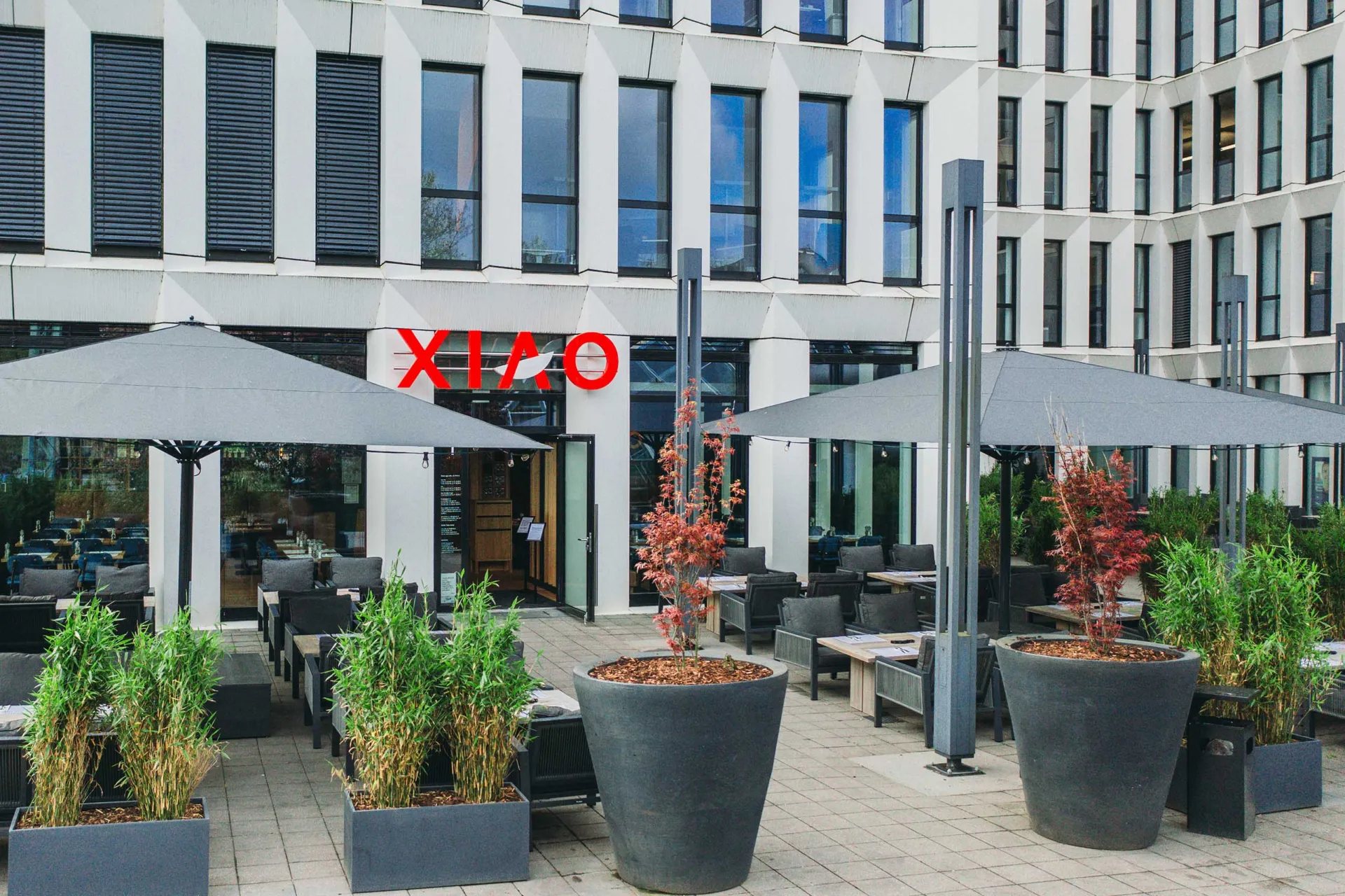 Eingang des XIAO Wuppertal mit Terrasse, Sonnenschirmen und Pflanzkübeln