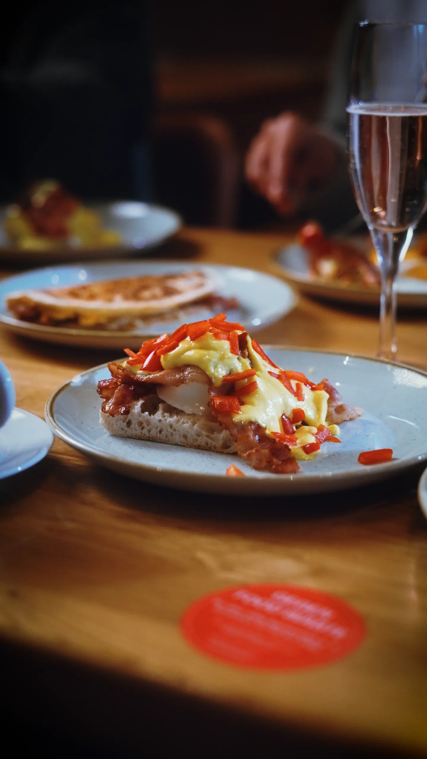 Brunch-Teller mit Eggs Benedict, Bacon und Sauce Hollandaise, im Hintergrund ein Glas Prosecco