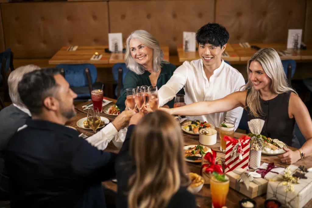 Gruppe stößt an einem festlich gedeckten Tisch im XIAO mit Getränken und Geschenken an
