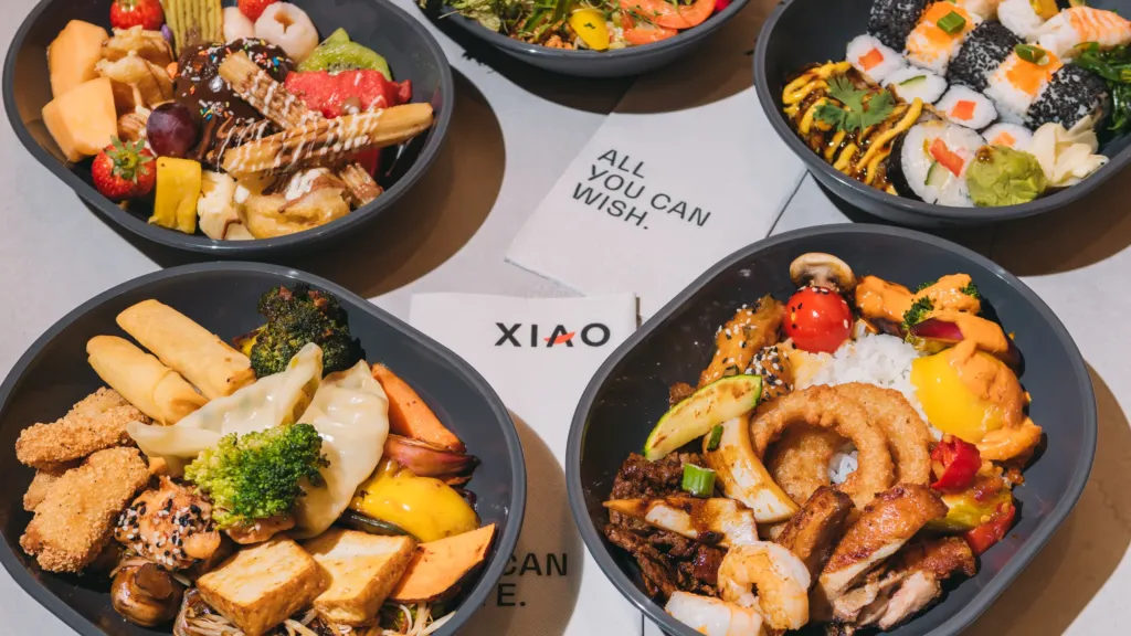 Mehrere Take-Away-Boxen mit Sushi, Wok-Gerichten, Fingerfood und Obst vom XIAO Erlebnis-Buffet
