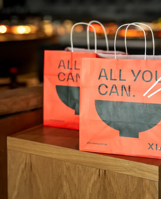 Zwei gebrandete Take-Away Papiertüten mit Essen zum Mitnehmen stehen zur Abholung bereit